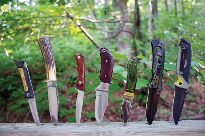 Row of fixed blade knives standing on a wooden rail in the woods