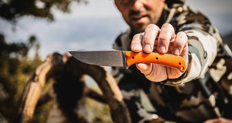 Hunter holding out a fixed blade knife with an orange handle