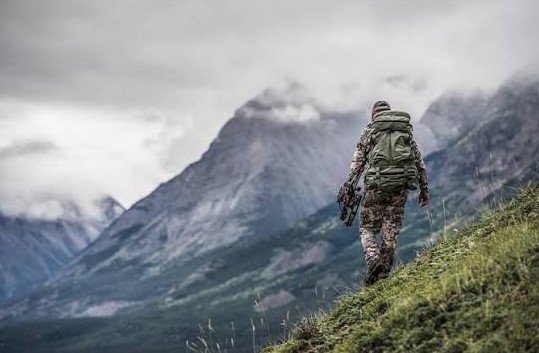 Hunter carrying a loaded pack up a steep mountain slope
